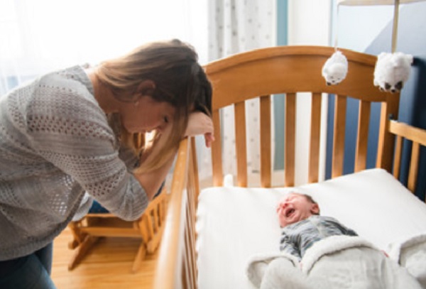 Уставшая мама сидит возле кроватки