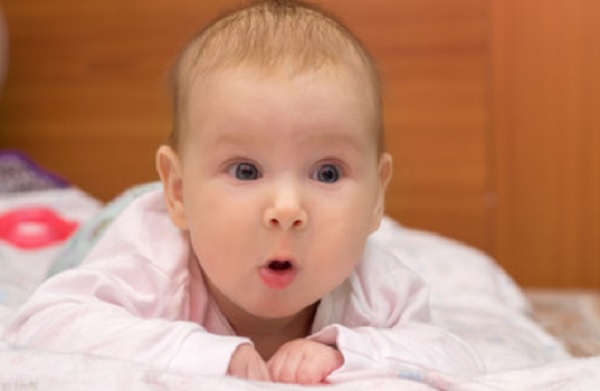 Грудной ребенок лежит на животе с открытым ротиком
