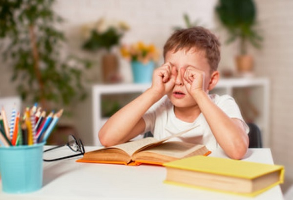 Ребенок трет глаза. На столе лежит книга