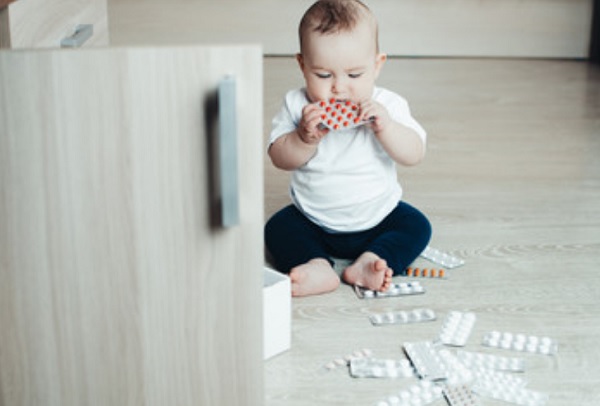 Возле ребенка на полу много таблеток. Он одну пластинку с лекарствами засовывает в рот