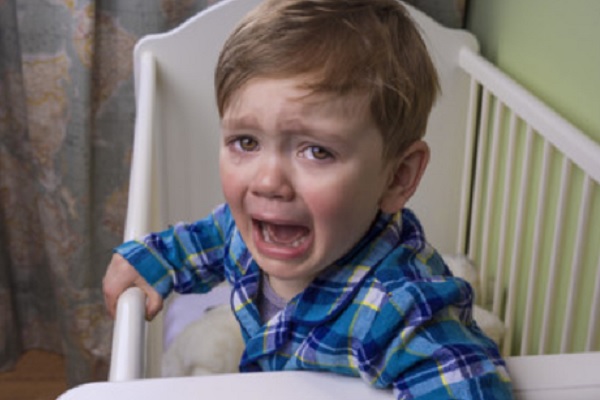 Ребенок стоит в кроватке и сильно плачет