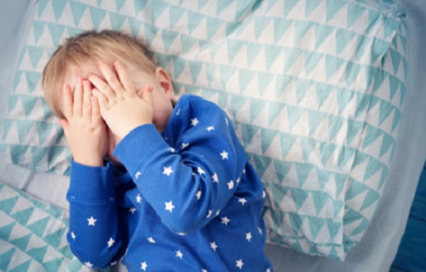 Ребенок лежит в кроватке, прикрывая лицо руками