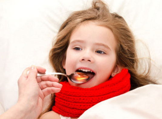 Девочке, которая лежит в постели дают сироп от температуры