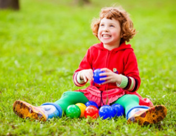 Девочка сидит на траве. Возле нее лежат маленькие мячики