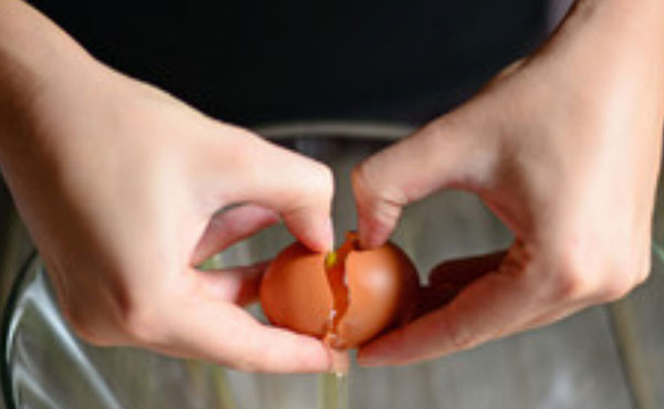 Над миской разбивают яйцо