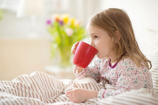 Девочка пьёт из чашки, находясь в постели