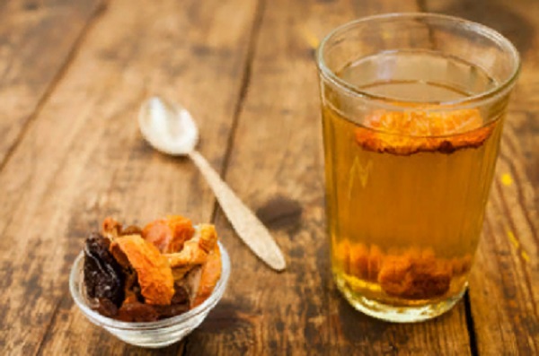 На столе стоит стакан с компотом из сухофруктов. Рядом лежит ложечка и маленькая креманка с сухофруктами