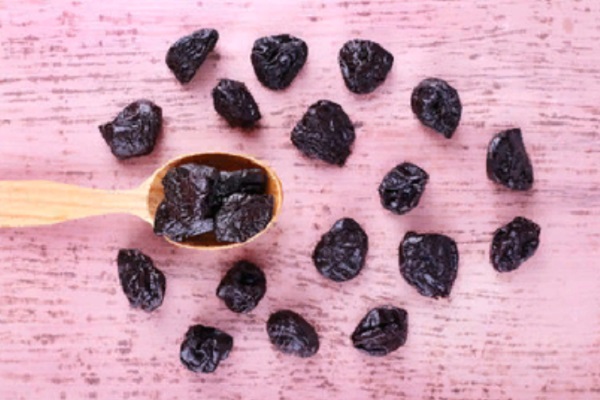 Мытый чернослив лежит на столе и на деревянной ложке