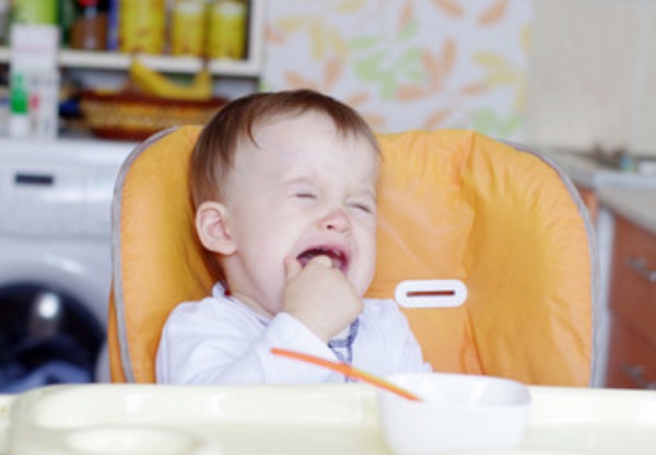 Маленький карапуз хныкает, сидя перед тарелкой