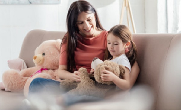 Мама с дочкой сидят на диване. У девочки в руках мягкая игрушка