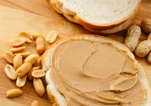 Хлеб, намазанный арахисовым маслом, рядом почищенный арахис