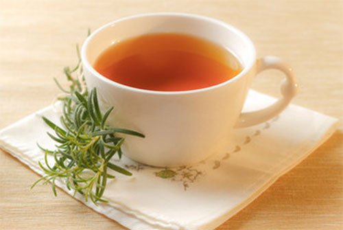 Настой розмарина в чашке, рядом лежит веточка растения