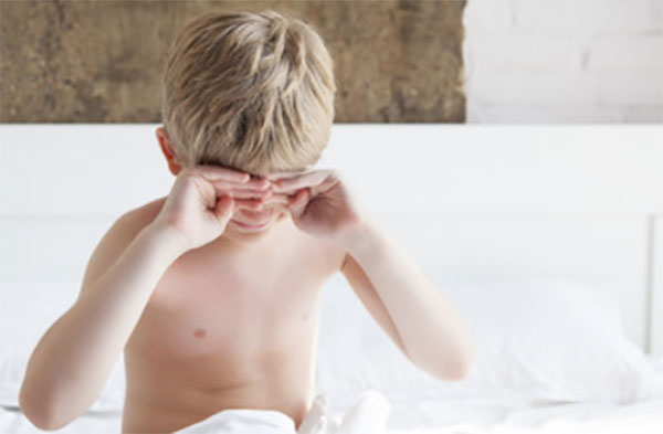 Мальчик сидит на кровати и потирает глаза, не может проснуться