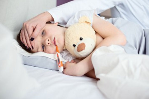 Ребенок лежит в постели с градусником во рту