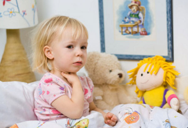 Девочка сидит в постели и держится за горло