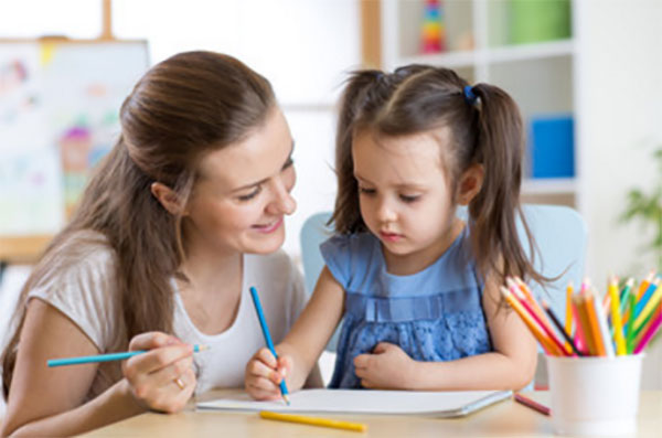 Девочка сидит возле мамы и рисует