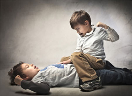 Один мальчик сидит на другом ребенке и собирается ударить его по лицу