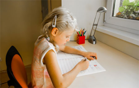 Девочка правильно сидит за столом и делает письменные уроки