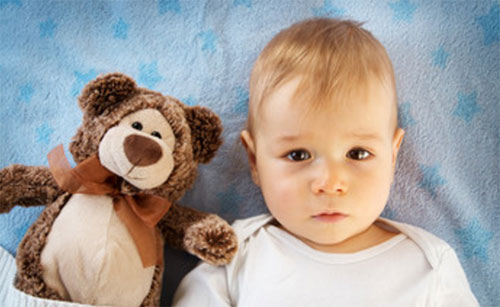 Ребенок лежит в постели, рядом с плюшевым медведем