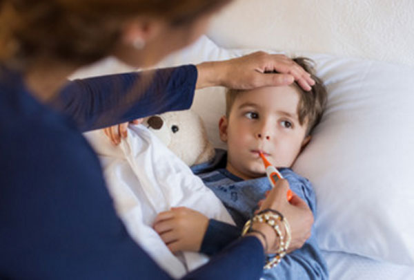 Ребенок лежит в постели с градусником во рту