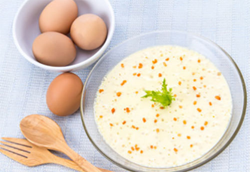 Паровой омлет, рядом лежит блюдо с сырым яйцами, деревянная ложка и вилка