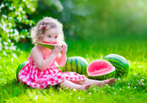Девочка сидит на траве и ест арбуз. Рядом несколько арбузов