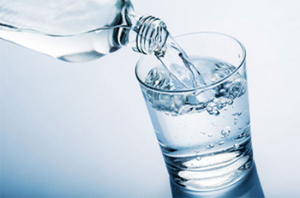 С бутылки наливают воду в стакан