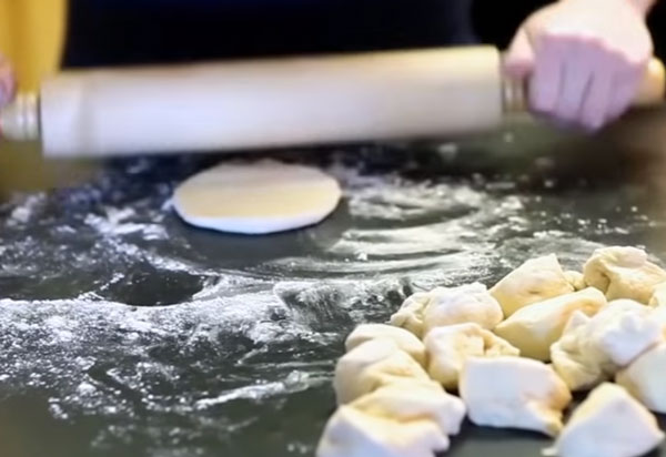 Тесто нарезано на кусочки. Один кусочек раскатывают скалкой