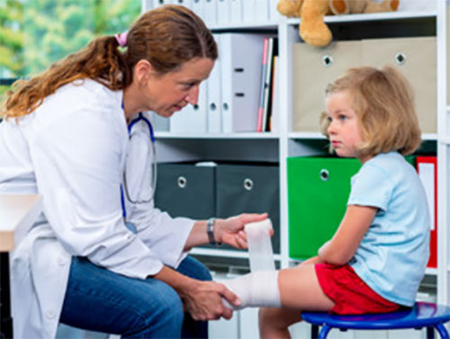 Врач обматывает бинтом ножку девочки