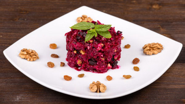 Блюдо с готовым салатом, украшенное грецкими орехами и изюмом