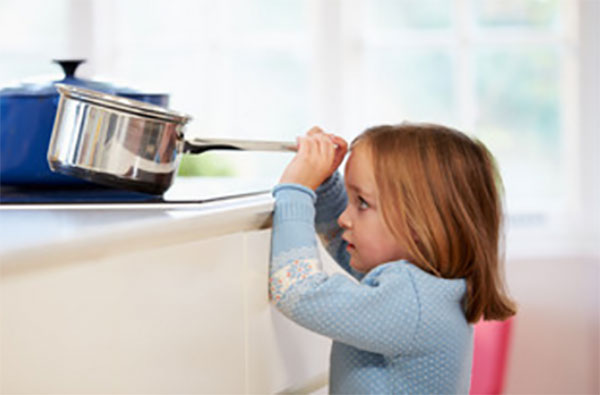 Девочка тянет ковшик с кипятком с плиты прямо на себя