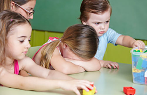 Девочка спрятала лицо, плачет. Рядом с ней серьезный мальчик, который по-видимому ее обидел и другие дети