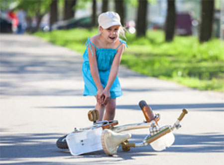 Девочка стоит возле перевернутого велосипеда и держится за коленко