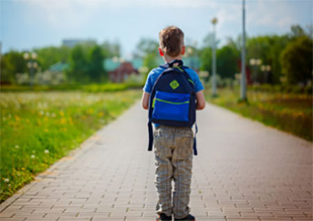 Идущий по тропинке мальчик с рюкзаком на плечах