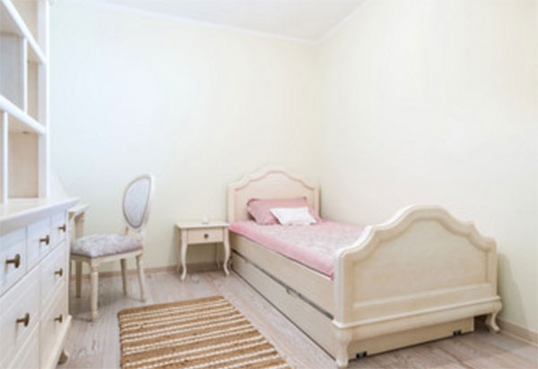 Светлая, простая комната. Кровать с рельефными спинками, простой шкаф, тумбочка, стул и дорожка