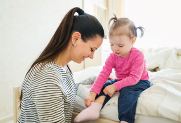 Девочка сама надевает носки. Мама смотрит на это и улыбается