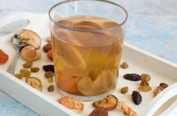 Компот из сухофруктов в стакане. Стакан стоит на подносе, вокруг него разложенные сухофрукты