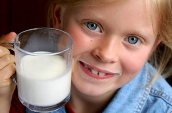 Девочка с молочными "усами" держит чашку молока