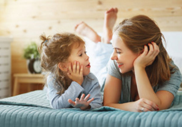 Мама с дочкой лежат на кровати. Девочка пытается что-то произнести