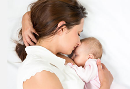 Мама лежит с грудничком, ребенок сосет грудь