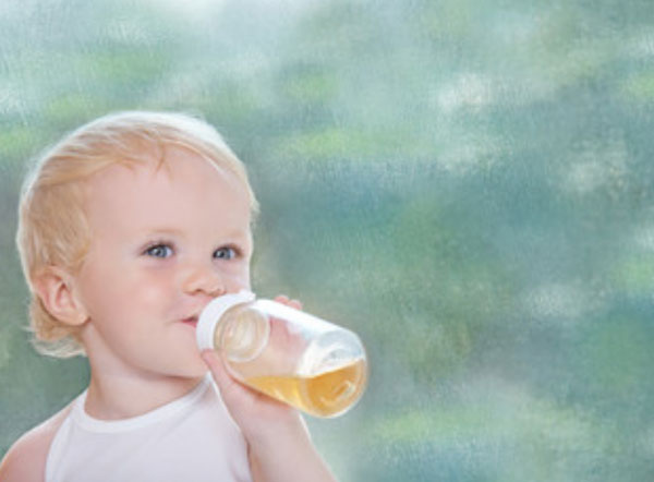 Маленький ребенок пьет яблочный сок с бутылочки