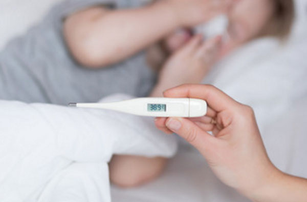 На переднем плане градусник с показанием 38,9. На заднем ребенок высмаркивает носик