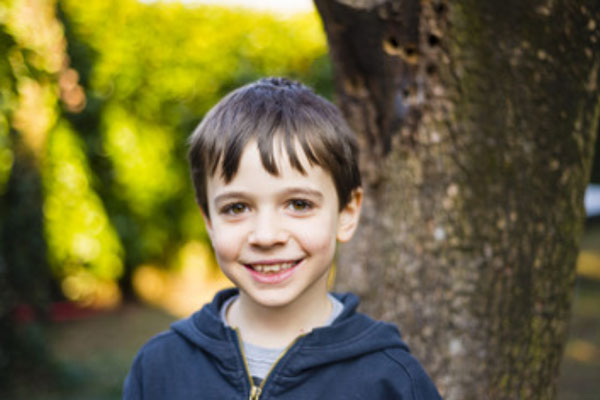 Улыбающийся мальчик стоит возле дерева