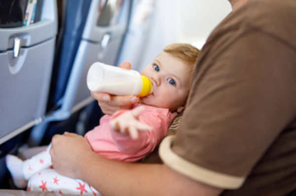 Ребенок сидит на руках родителя и пьет с бутылочки молоко