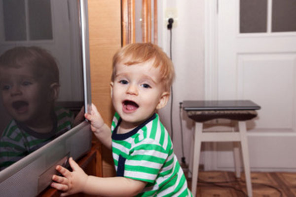 Мальчик стоит возле выключенного телевизора, пытается его включить