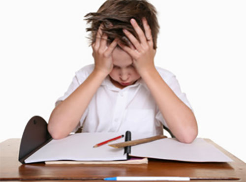 Мальчик держится за голову от бессилия. Перед ним на столе уроки