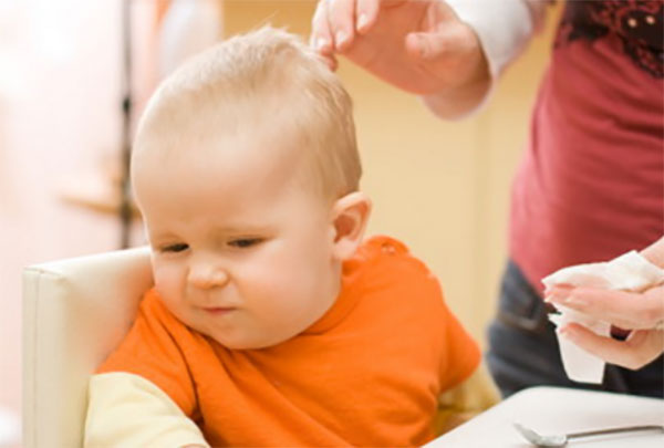 Маленькому ребенку мама пытается втереть масло в волосы, а он отворачивается