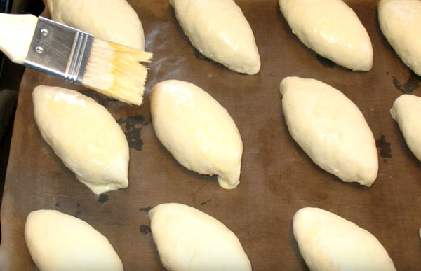 Сырые пирожки на противне смазывают яйцом