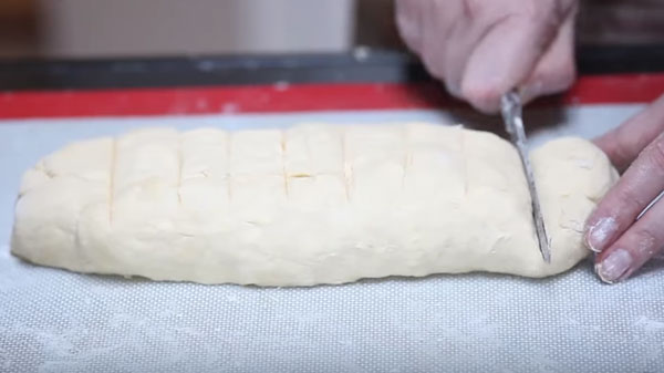 Колбаску из теста разметили на девять кусков, начинают первый отрезать