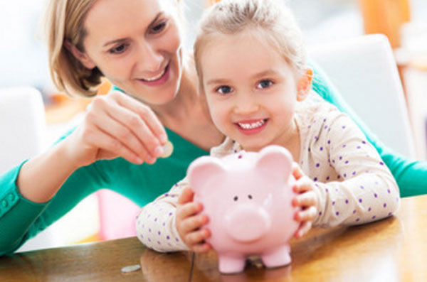 Девочка держит копилку. Мама кладет в нее монетки